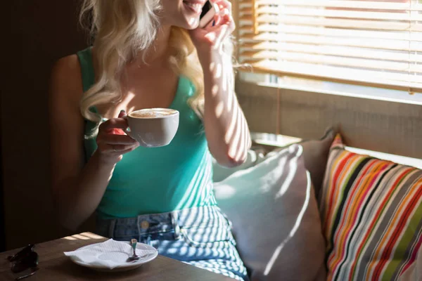Mutlu kadın içecekler kahve ve gülümsüyor pencere panjur ile yakın:.