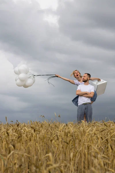 Coppia con le palle e una valigia sui campi Paul con forte vento — Foto Stock