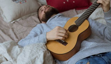 Genç Modern adam yatağa gitar çalmak. Kopya alanı