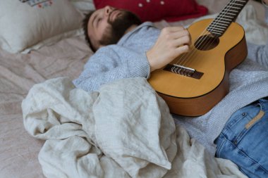 Genç Modern adam yatağa gitar çalmak. Kopya alanı