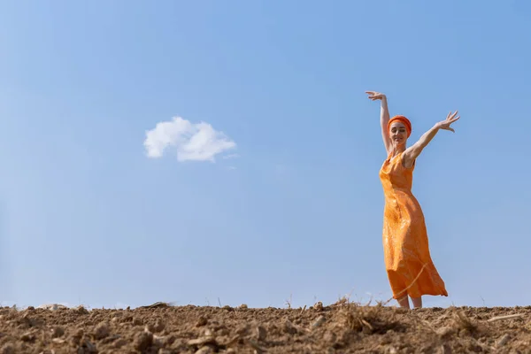 Etnická žena v turbanu tančí na čisté půdě na obloze a na pozadí mraků — Stock fotografie