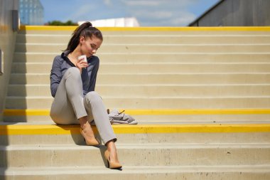 Bir tek kullanımlık kahve fincanı ile güzel genç iş kadını kentsel şehir arka plan karşı kahve içme.