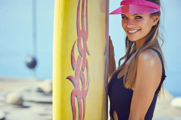若いセクシーな女性長い毛と 陽気な日焼けボディ ビーチ サーフィンのための準備にサーフィン ボードを浮かべてします 手を振っています 肯定的な感情 — ストック写真