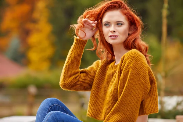 秋の公園で木製のテラスでリラックスした赤髪の女性 — ストック写真