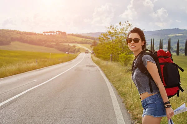 国の道路の上を歩いてのバックパックを運ぶ美しい旅行者女性 — ストック写真