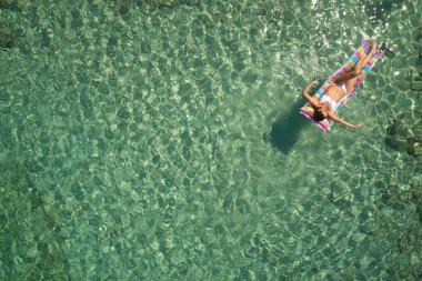 Yukarıdan aşağıya bir hava yatağı üzerinde yüzen bir güzel kadının beyaz bir bikini görünümü 