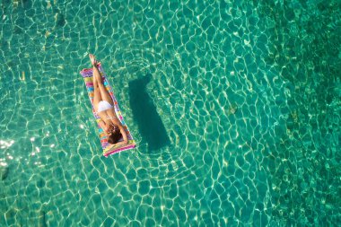 Yukarıdan aşağıya bir hava yatağı üzerinde yüzen bir güzel kadının beyaz bir bikini görünümü 