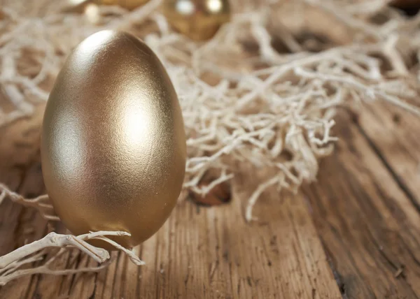 Goldene Ostereier im Nest auf rustikalem Holzgrund — Stockfoto