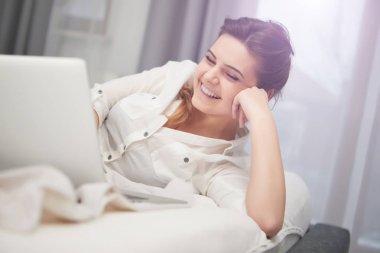 Aydınlık ve rahat yatak evde yatakta yatan dizüstü bilgisayar ile çalışan genç kadın