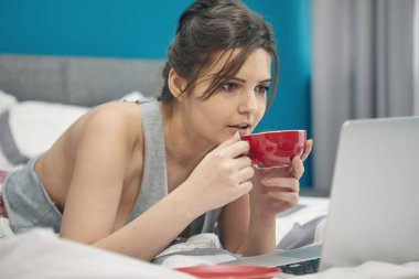 Evdeki yatağın üzerinde dizüstü bilgisayarda çalışan mutlu ve güzel bir kadın.. 