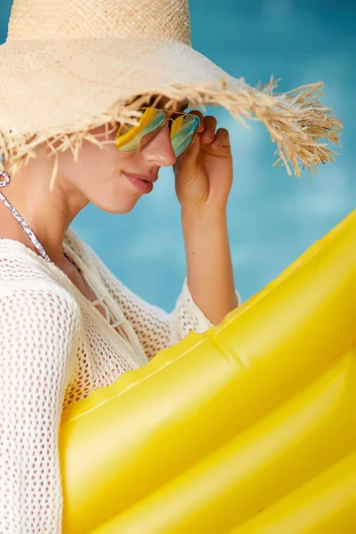 Fashion beautiful woman on summer vacation relaxing at luxury resort spa poolside. Young fashionable lady wearing sun hat