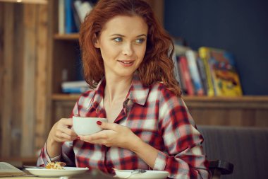 Öğrenci Kitaplığı'nda bir kitap okur ve kahve içer