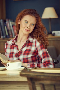 Öğrenci Kitaplığı'nda bir kitap okur ve kahve içer