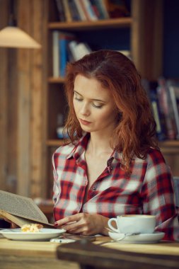 Öğrenci Kitaplığı'nda bir kitap okur ve kahve içer