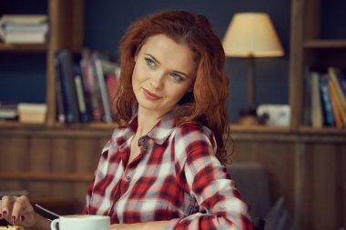 Öğrenci Kitaplığı'nda bir kitap okur ve kahve içer