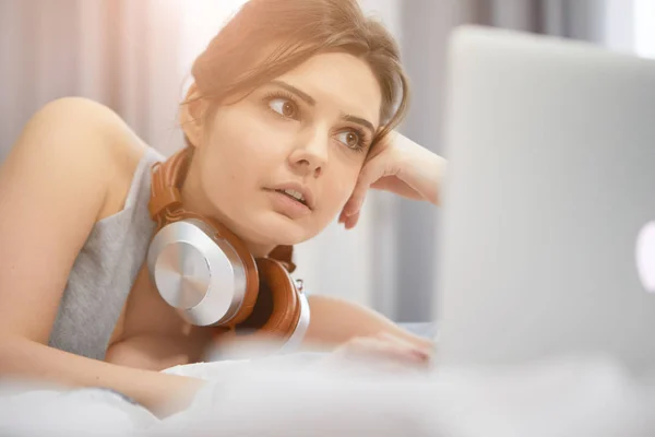 Žena používající přenosný počítač a naslouchající sluchátky při lhaní — Stock fotografie