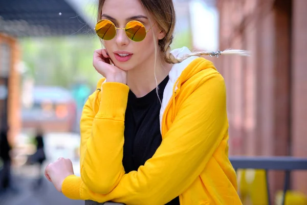 Hermosa mujer en una sudadera amarilla y gafas de sol en el st — Foto de Stock