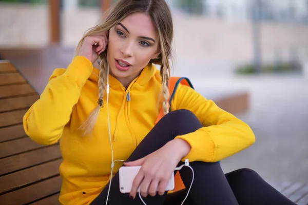 Jovem mulher em roupas esportivas descansando e ouvindo música no smar — Fotografia de Stock