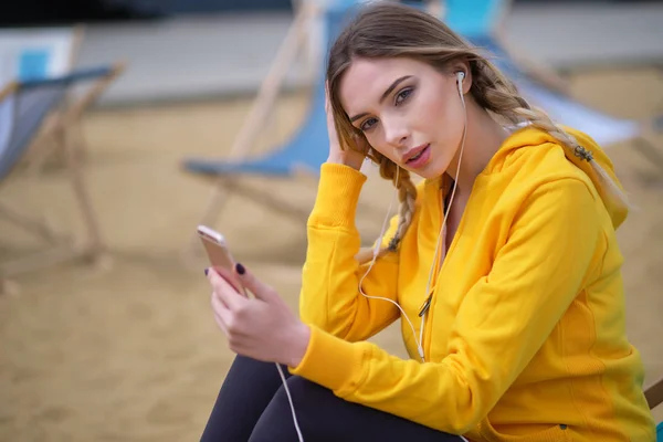 Mujer joven en traje deportivo descansando y escuchando música en smar — Foto de Stock