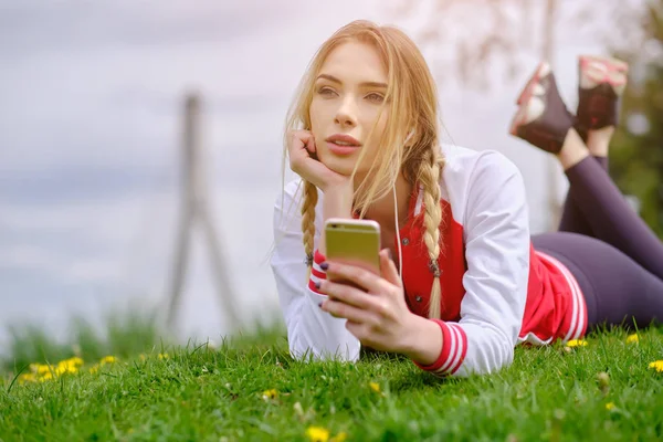 Mulher com fones de ouvido e smartphone ouvindo música na grama . — Fotografia de Stock