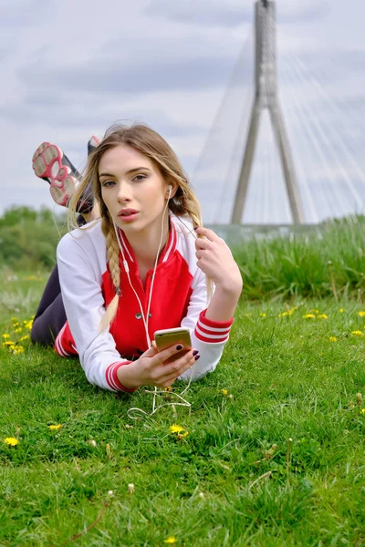 Mujer con auriculares y smartphone escuchando música sobre hierba . — Foto de Stock