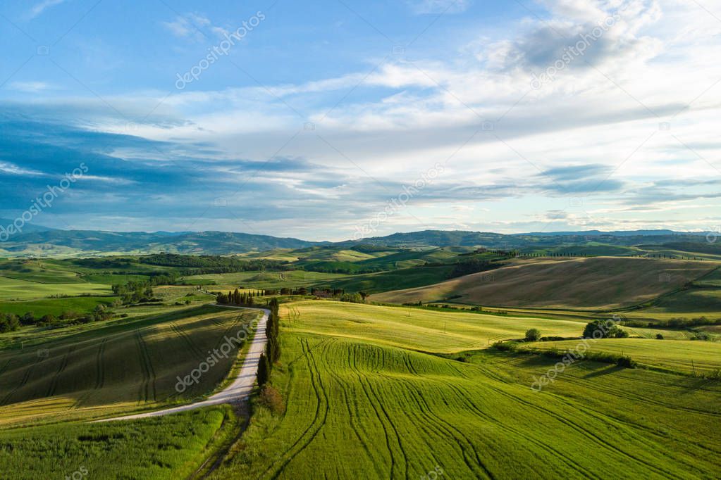 Picturesque Tuscany landscape with rolling hills, valleys, sunny fields, cypress trees along winding rural road, houses on a hill. Tourist visit in Tuscany 