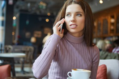 Kafede mesajları okuyan genç bir kadın resmi.