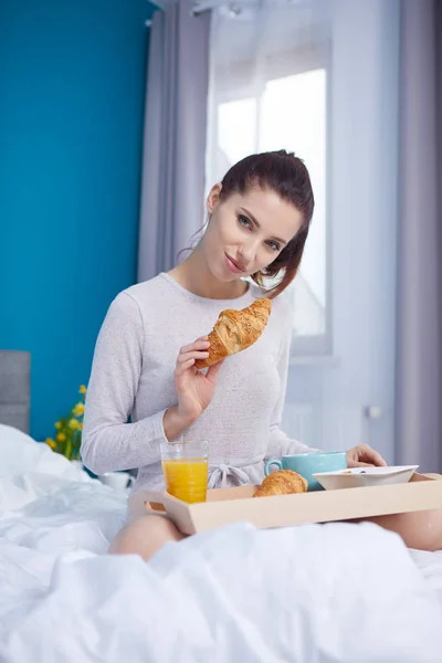 Attraktiv kvinna äta spannmål sitter på sängen hemma — Stockfoto