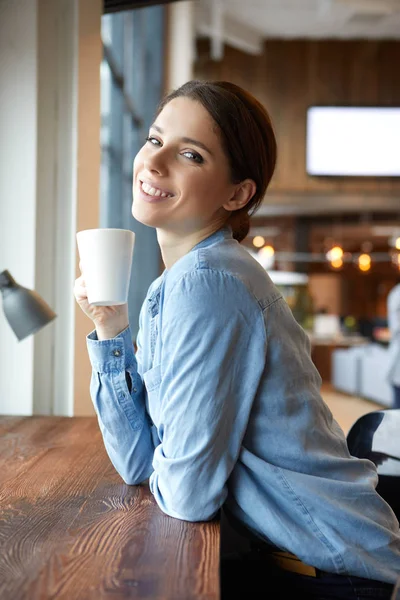 Μια νεαρή γυναίκα πίνει καφέ στο γραφείο. — Φωτογραφία Αρχείου