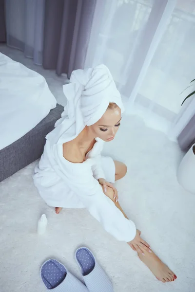 Jolie blonde utilisant de la crème pour le corps sur le lit à la maison — Photo