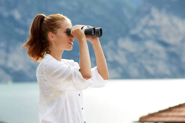 Tourist woman on top of the mountain looking through binoculars