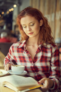 Kız bir kafede kahve içip kitap okuyor.