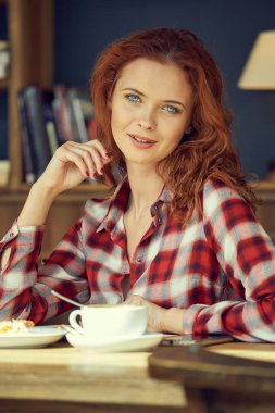 Kız bir kafede kahve içip kitap okuyor.