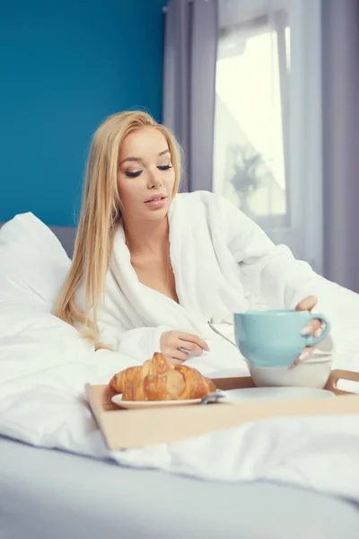 Νεαρή όμορφη γυναίκα παίρνει πρωινό στο κρεβάτι. — Φωτογραφία Αρχείου