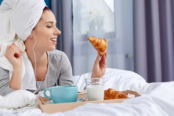 Menina com uma toalha na cabeça tomando café da manhã na cama — Fotografia de Stock