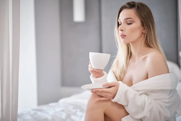 Frau im Bademantel trinkt Morgenkaffee im Bett — Stockfoto