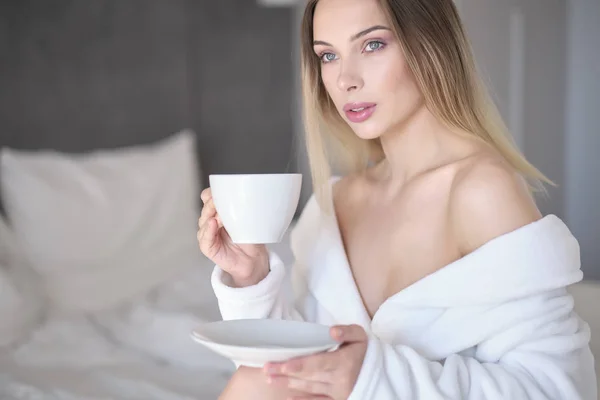 Frau im Bademantel trinkt Morgenkaffee im Bett — Stockfoto