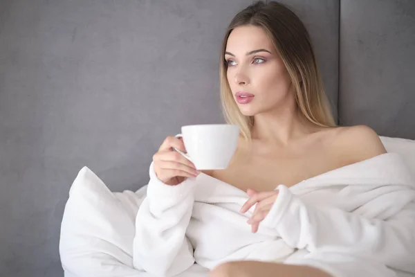 Mujer en un albornoz bebe café de la mañana en la cama — Foto de Stock