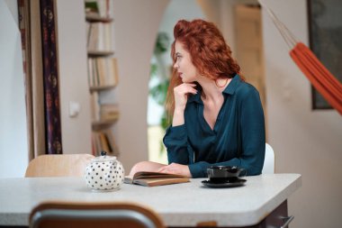 Evdeki pencerenin yanında kitap okuyan güzel genç bir kadın.