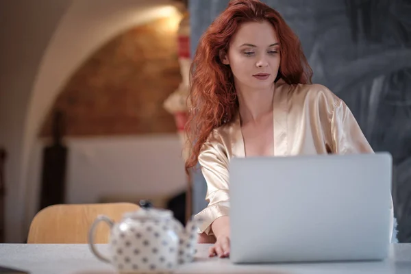 Vrouw in een badjas werkt op een laptop thuis — Stockfoto