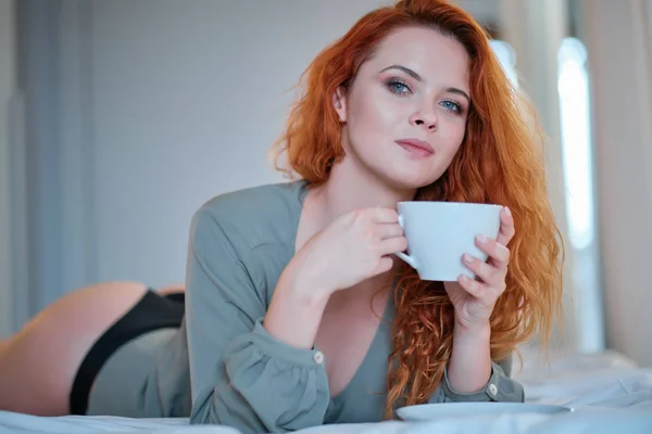 손에 커피를 들고 집에 있는 사물함에 앉아 있는 한 여자 — 스톡 사진