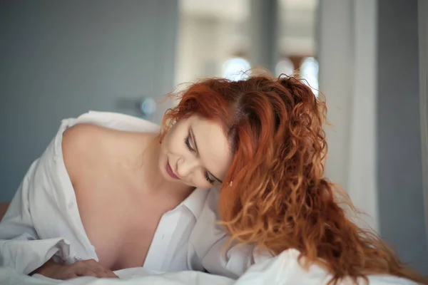 En kvinna i en mans skjorta ligger på sängen. — Stockfoto