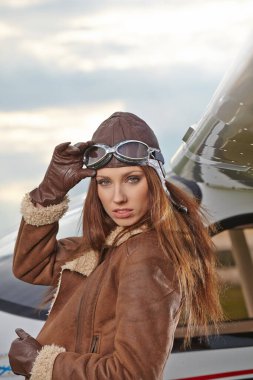 Gülümseyen Genç Kadın Pilot Portresi. Özel uçağın önünde duran güzel genç kadın pilotun portresi. Arka planda modern küçük uçakları olan kadın pilot..