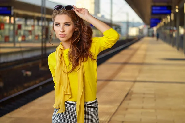 黄色の旅行スーツケースを着た女性が駅で電車を待っています — ストック写真
