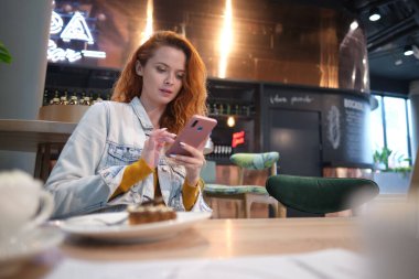 Alışveriş merkezindeki kafede oturmuş akıllı telefon kullanan gülümseyen genç bir kadının portresi..