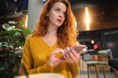 Alışveriş merkezindeki kafede oturmuş akıllı telefon kullanan gülümseyen genç bir kadının portresi..