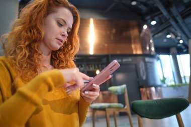 Alışveriş merkezindeki kafede oturmuş akıllı telefon kullanan gülümseyen genç bir kadının portresi..