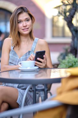 Bir kadın eski şehrin caddesindeki bir kafede akıllı telefon kullanıyor.