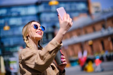 Kapanış mutlu hippi kız dışarıda cep telefonuyla selfie çekiyor. Şehir caddesinde cep telefonu tutan neşeli bir kadın. Arka planda cep telefonuyla gülümseyen kadın..