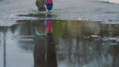 Yavaş çekim bacaklar bir koşucunun spor ayakkabı içinde kapatın. Çamurlu su birikintisi içine adım kadın spor adam açık havada bir parkta koşu.